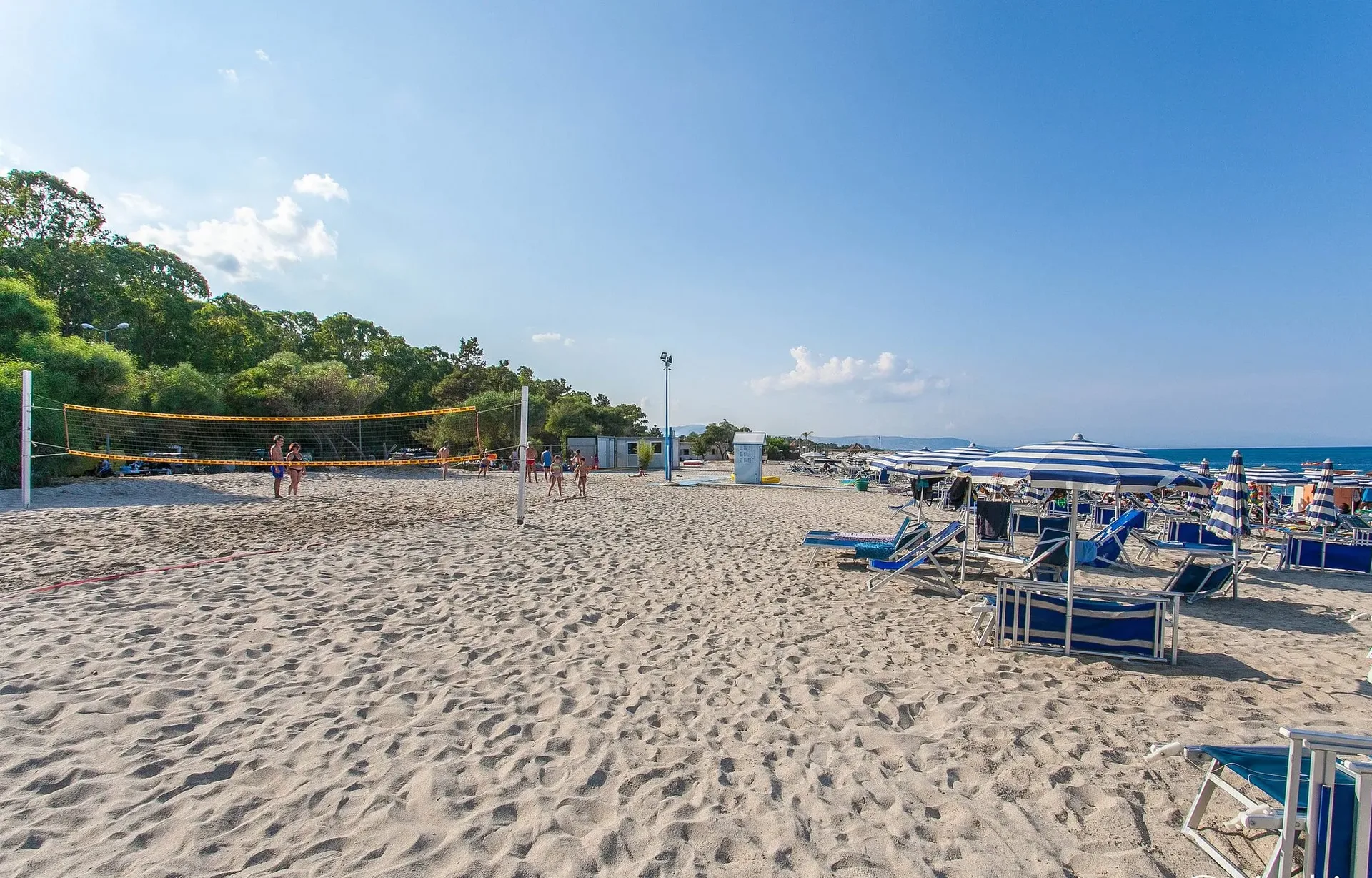 Spiaggia con campo da beach volley, ombrelloni a righe e lettini blu