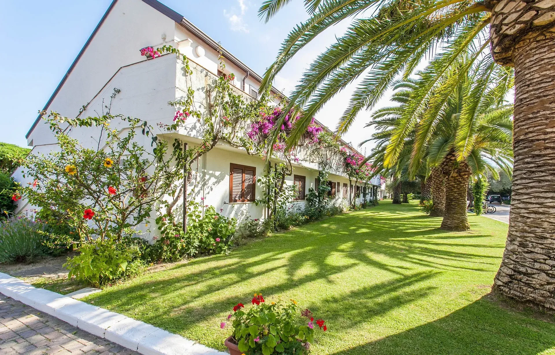Esterno degli alloggi bianchi con giardini fioriti e palme del villaggio