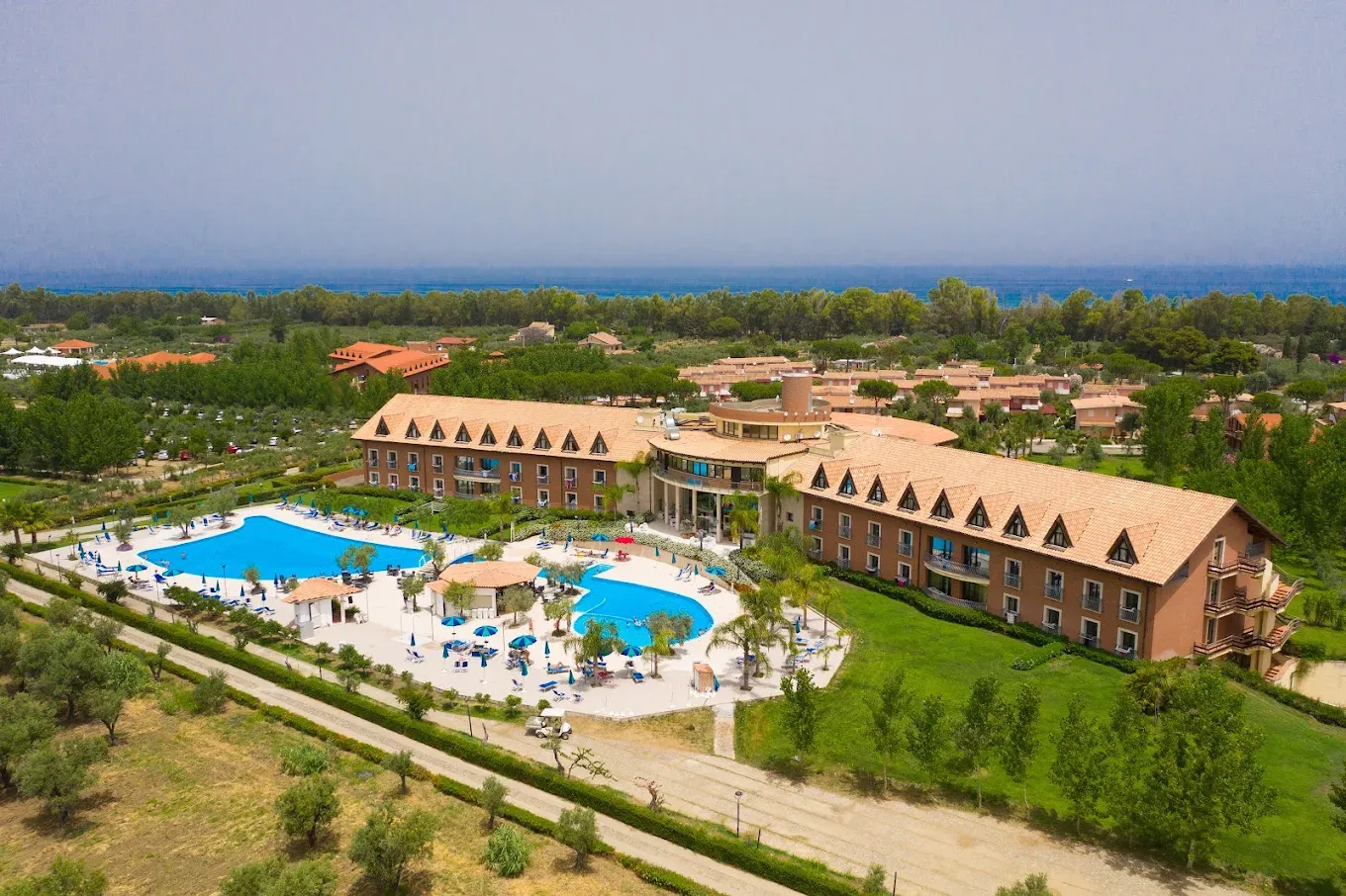 Vista aerea del resort con due piscine, edifici in mattoni e mare in lontananza