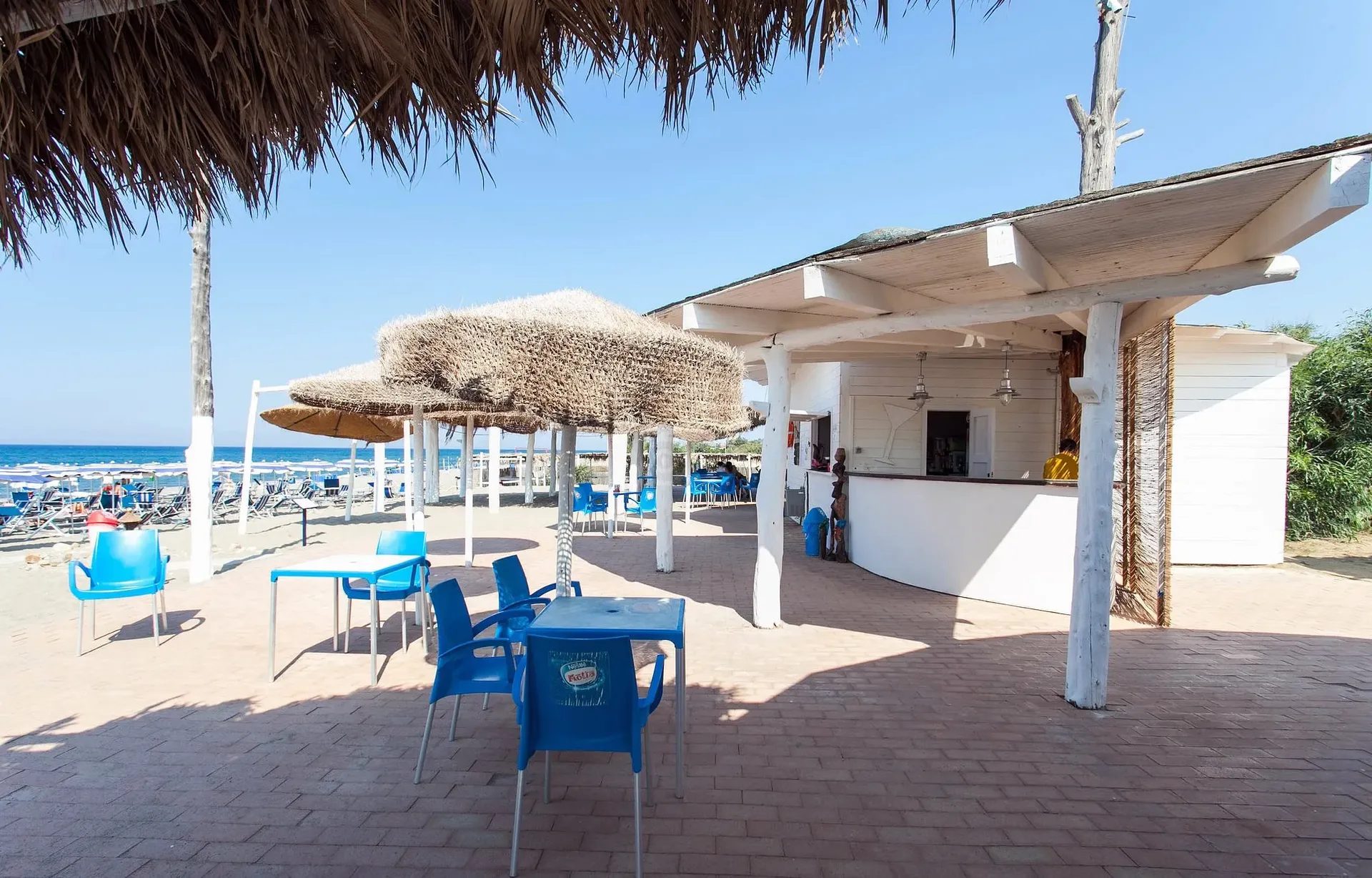 Bar sulla spiaggia con capanna in legno, ombrelloni in paglia e vista sul mare