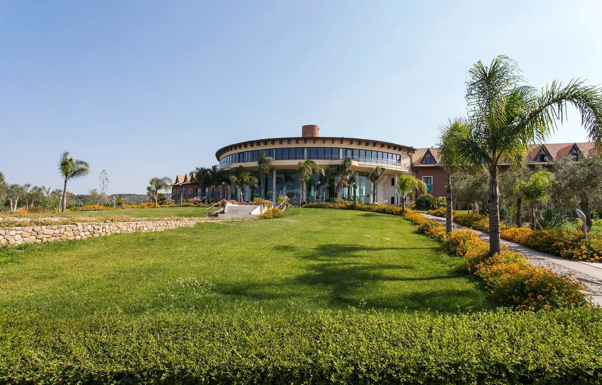 Edificio principale del resort con corpo circolare vetrato, prato verde e palme