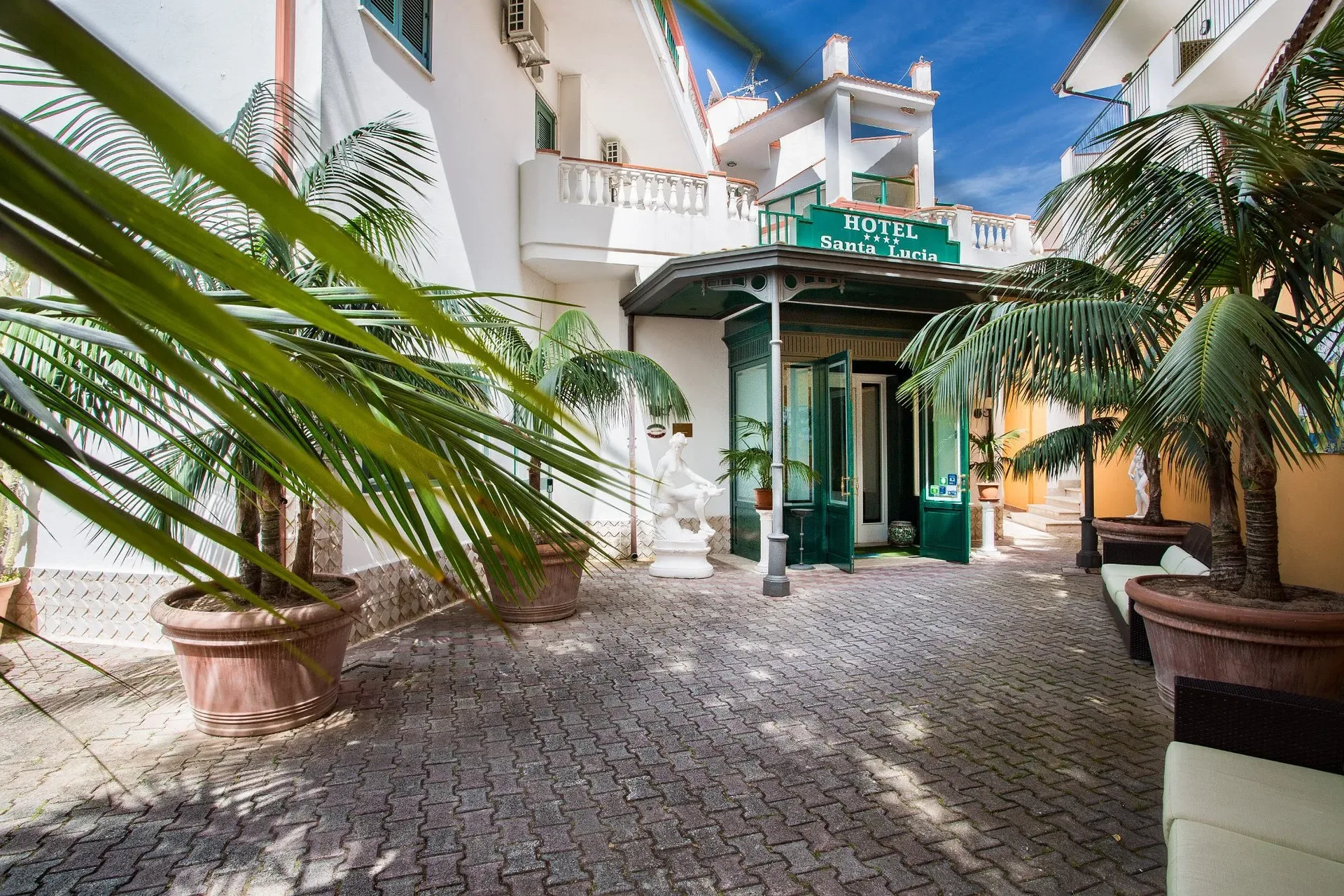 Ingresso dell'hotel Santa Lucia con palme in vaso e statue