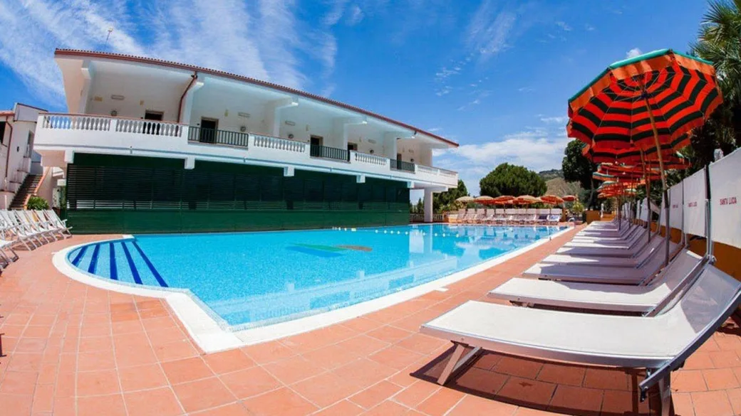 Piscina con lettini e ombrelloni a righe accanto all'edificio dell'hotel