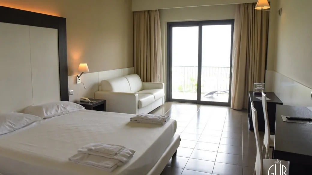 Camera con letto matrimoniale, divano e ampia vetrata sul balcone vista mare