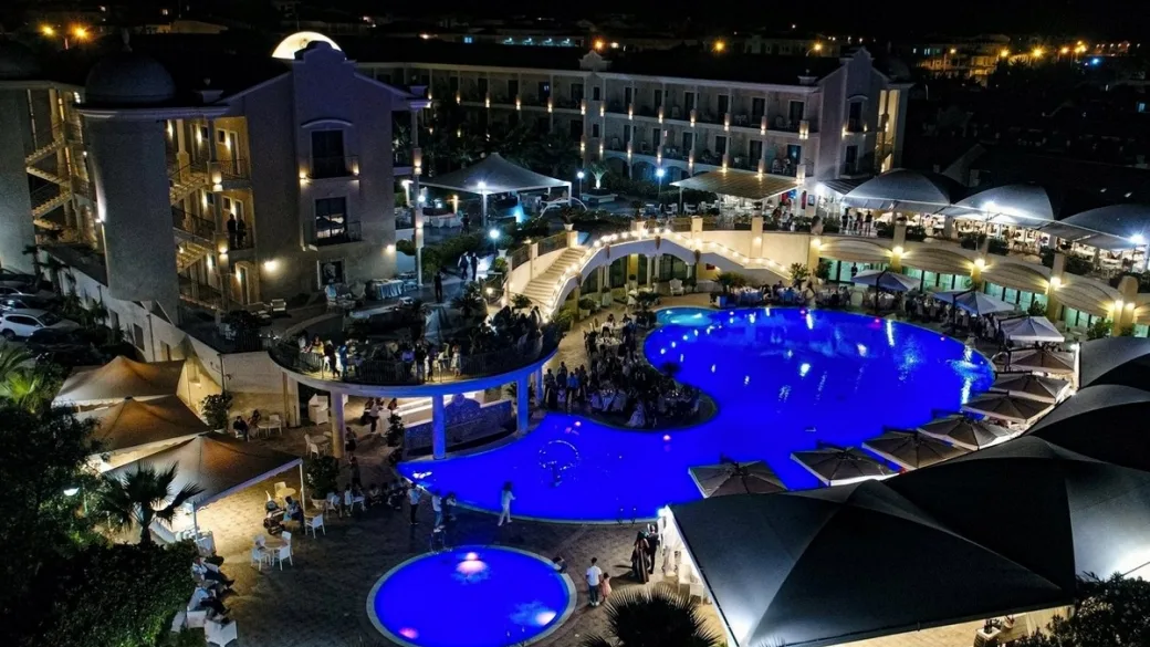 Resort illuminato di notte con piscina blu e evento all'aperto