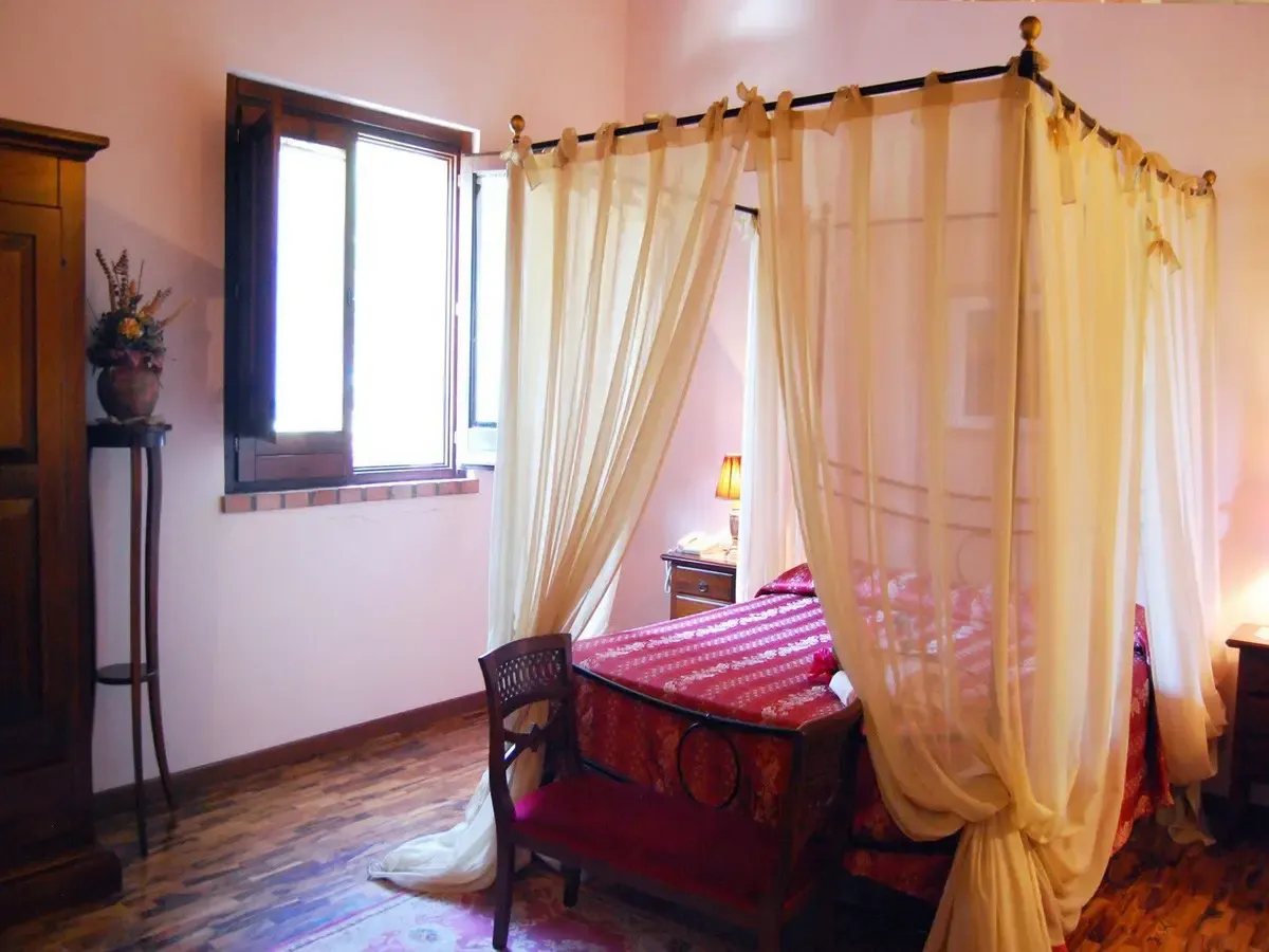 Camera con letto a baldacchino, tende drappeggiate e arredi in legno