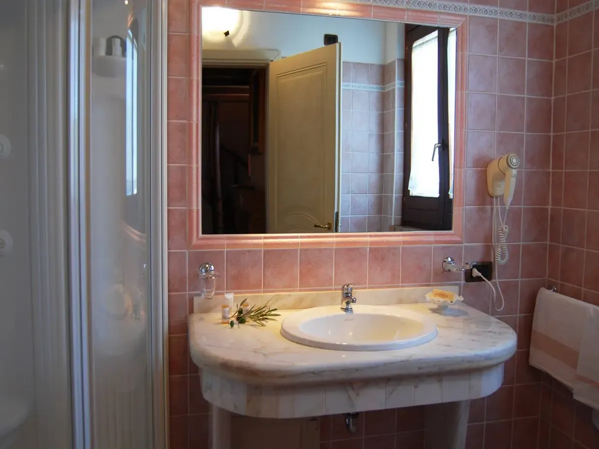 Bagno con piastrelle rosa, lavabo in marmo e specchio