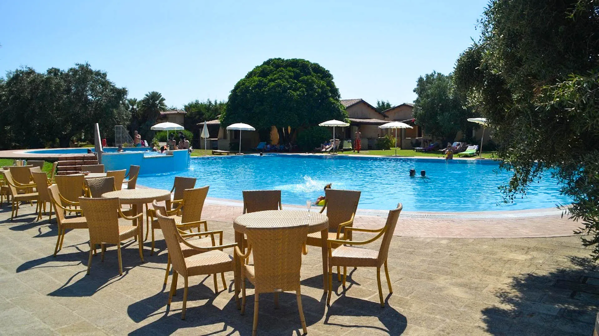 Bordo piscina con tavoli e sedie in vimini e persone che si rilassano in acqua