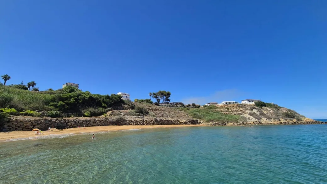 Spiaggia sabbiosa con mare turchese e costa rocciosa con vegetazione