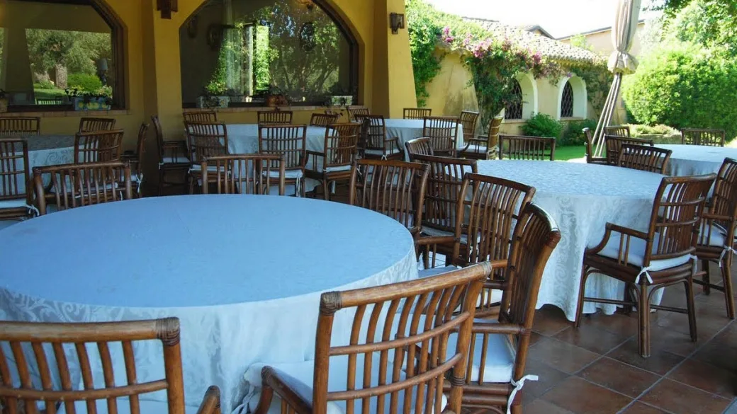 Terrazza ristorante con tavoli rotondi apparecchiati e sedie in vimini