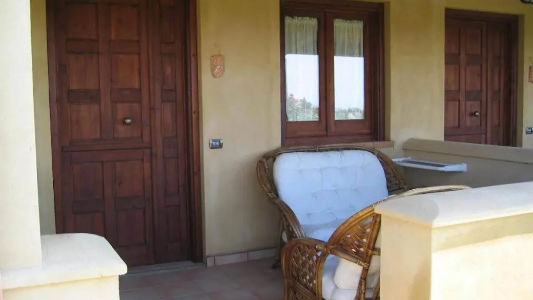 Portico esterno della camera con poltrona in vimini e porte in legno
