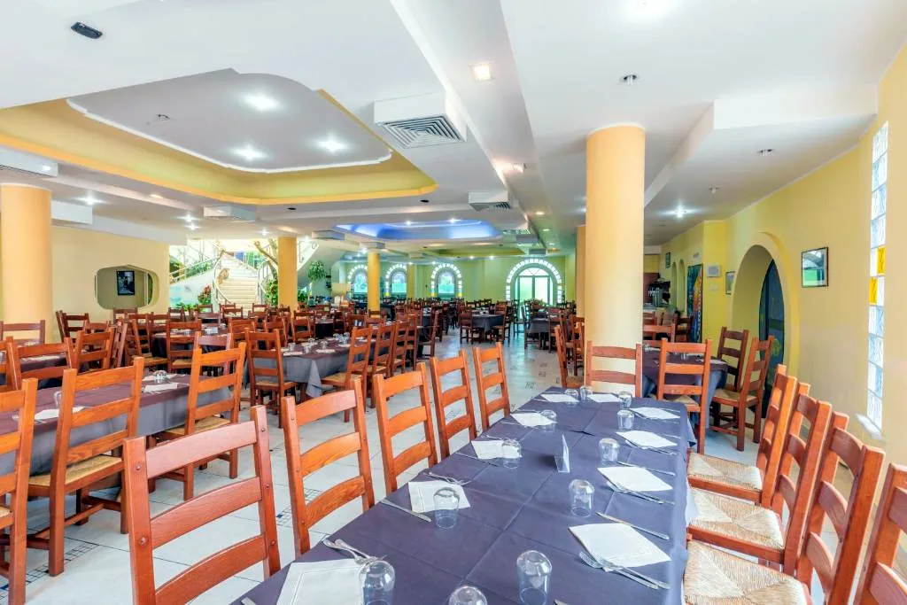 Ampia sala ristorante con tavoli apparecchiati, sedie in legno e colonne gialle