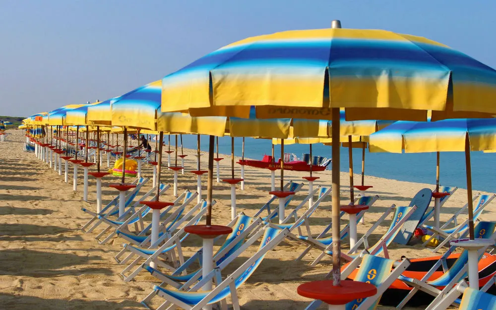 File di ombrelloni gialli e blu con lettini colorati sulla spiaggia