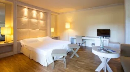 Camera d'albergo moderna con letto matrimoniale, illuminazione calda, tavolo rotondo, due sgabelli e scrivania con sedia.