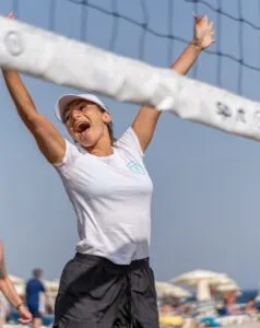 Donna felice che gioca a beach volley in spiaggia con rete e ombrelloni sullo sfondo.
