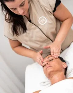 Una donna riceve un massaggio facciale mentre è sdraiata su un lettino; l'operatrice si concentra sulla sua fronte.