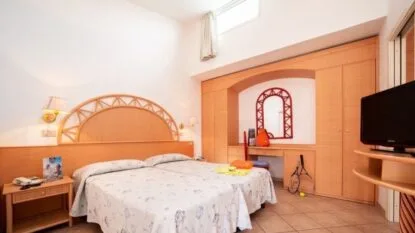 Camera da letto con due letti singoli uniti, armadio in legno, specchio e televisore su mobile.