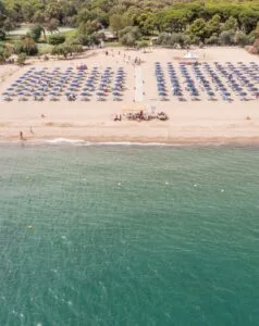 Spiaggia con ombrelloni blu e lettini ordinati, mare calmo e persone che passeggiano sulla riva sabbiosa.