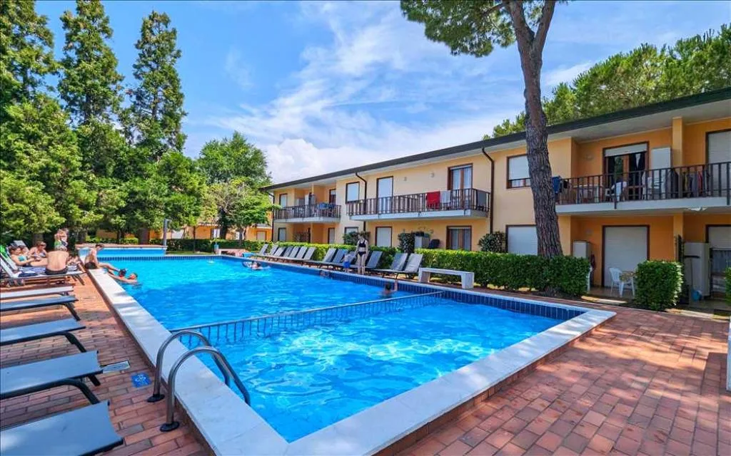 Ampia piscina all'aperto con lettini e residence a due piani giallo