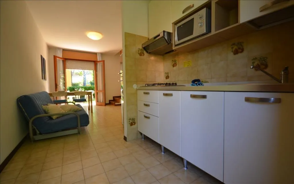 Cucina con mobili bianchi, divano e affaccio sul giardino privato