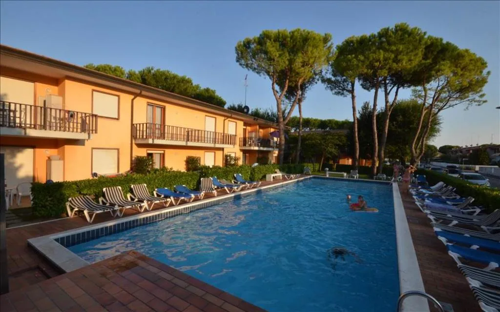 Piscina al tramonto con lettini e residence giallo circondato da pini