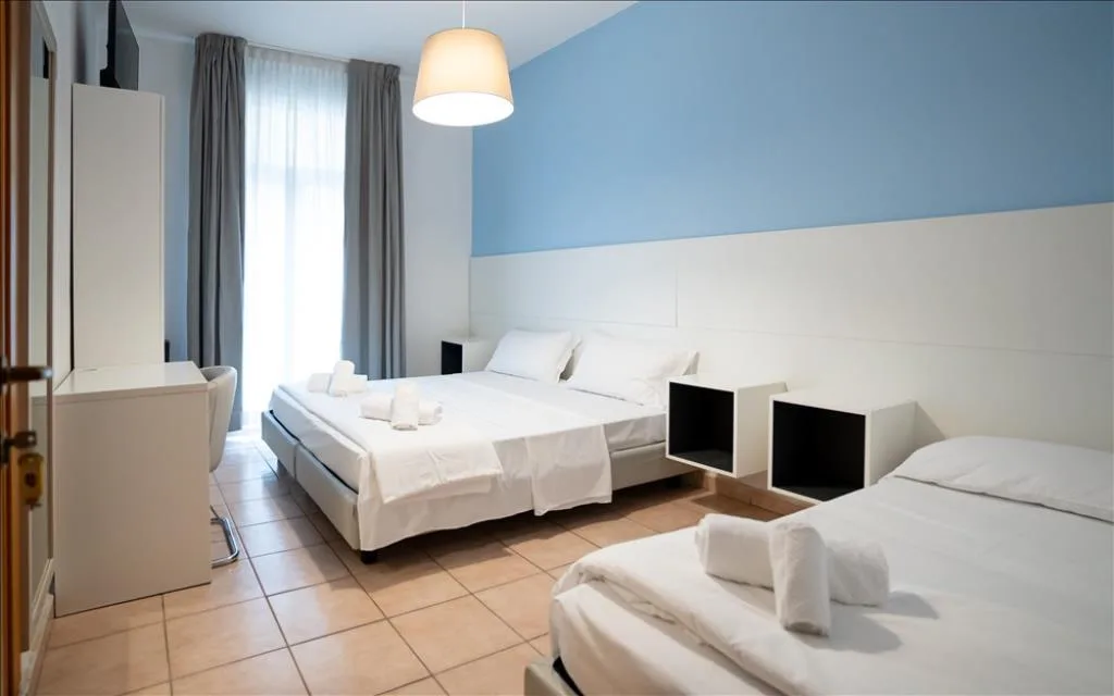 Camera tripla con due letti, parete azzurra e ampia finestra con tende grigie