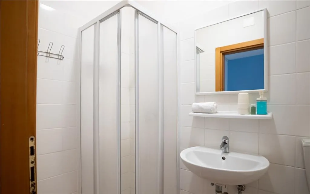 Bagno con box doccia, lavabo e specchio, ambiente luminoso con piastrelle bianche