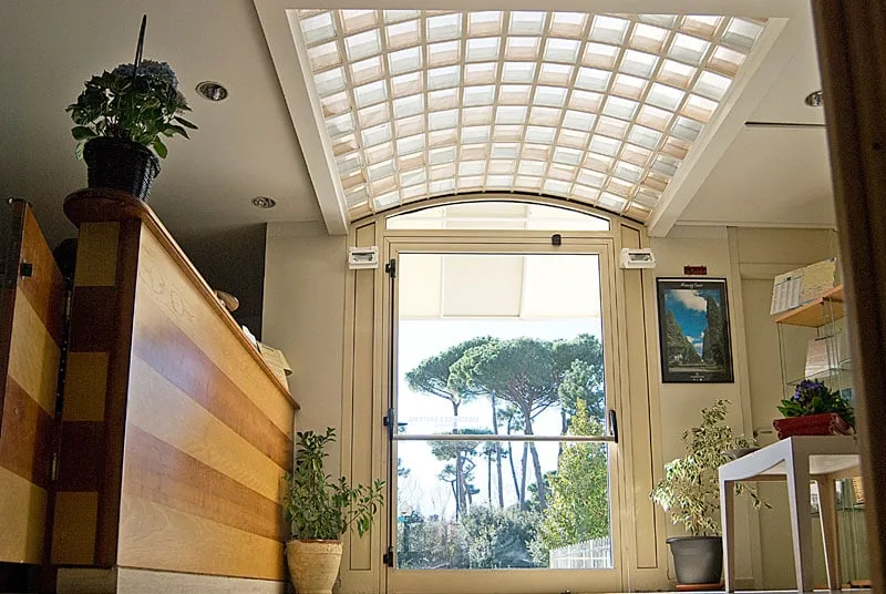 Ingresso della hall con soffitto a lucernario e vista sui pini esterni