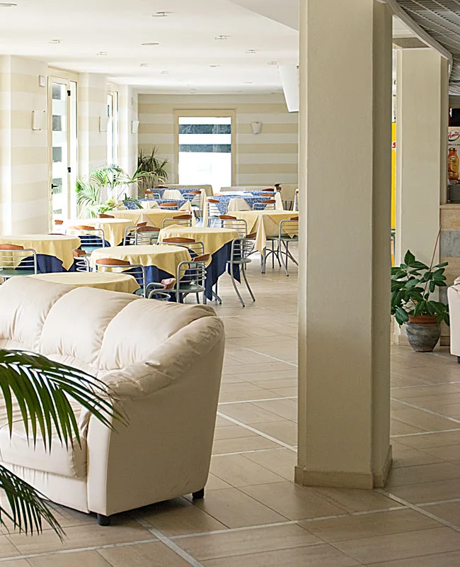 Sala ristorante con tavoli apparecchiati e poltrona bianca in primo piano