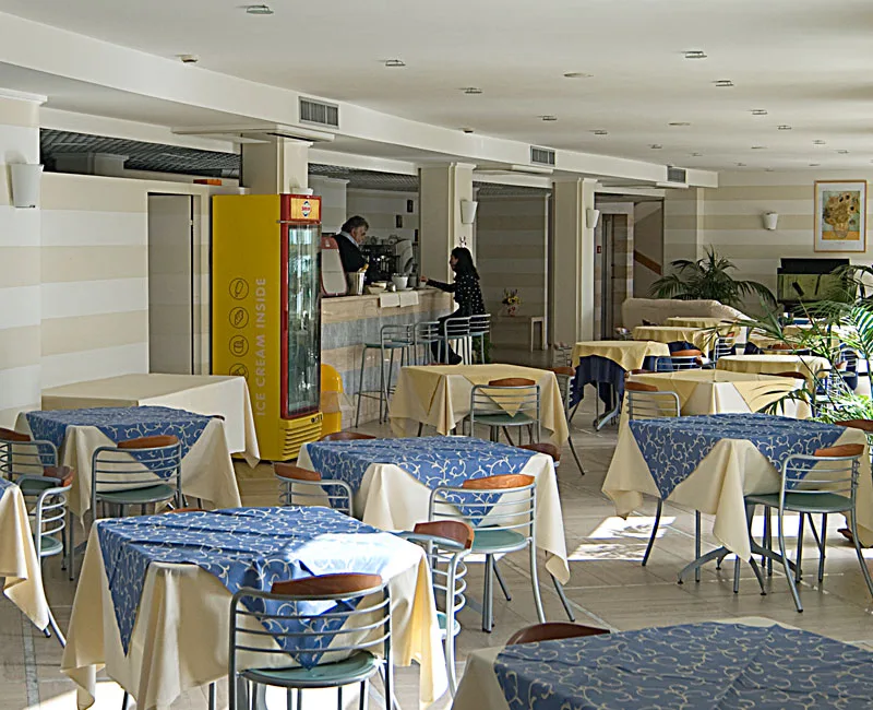 Sala colazione e bar con tavoli apparecchiati con tovaglie blu e gialle