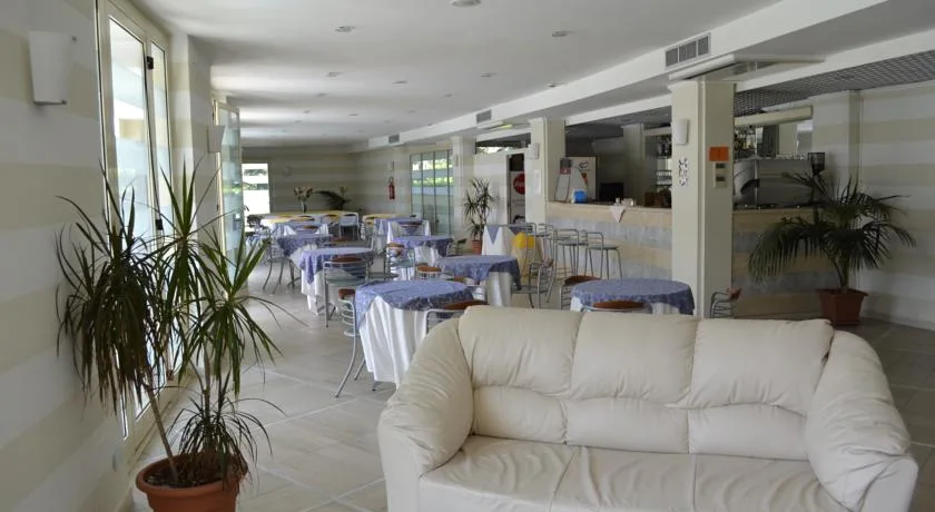 Sala ristorante luminosa con divano bianco, tavoli e area bar