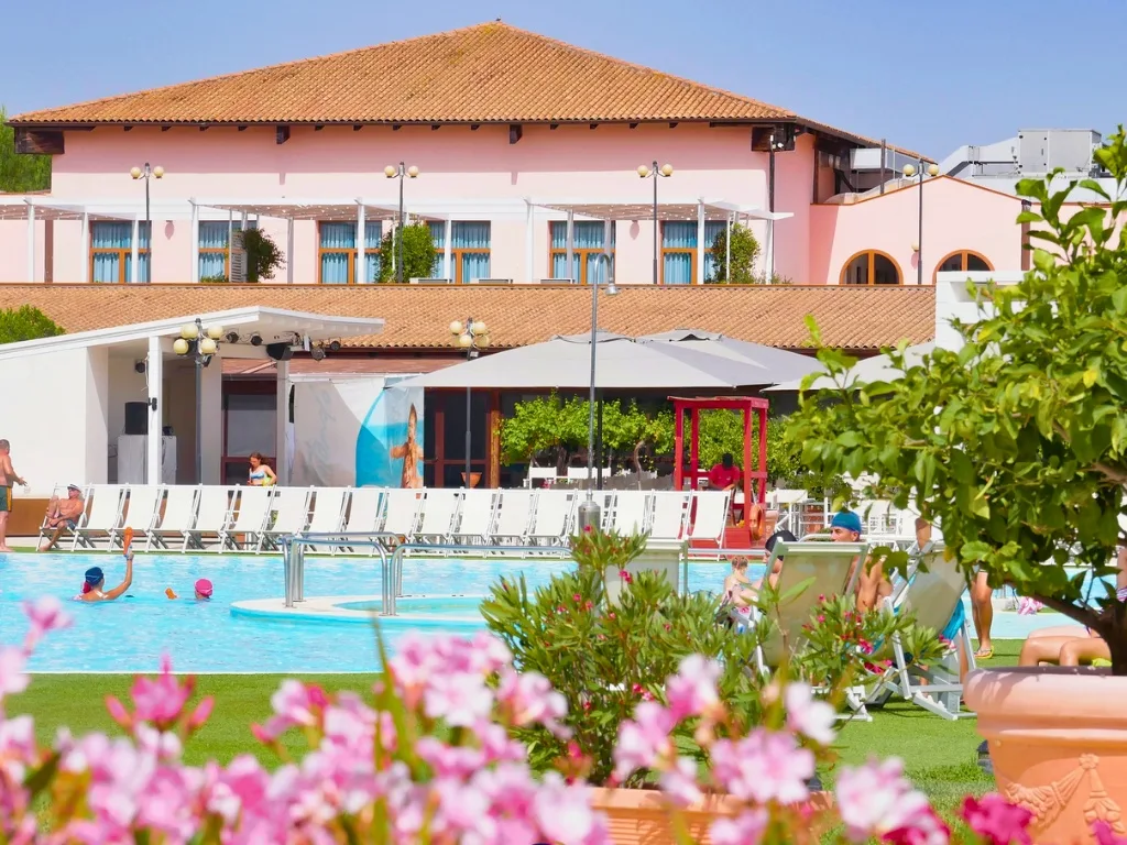 Piscina con lettini e fiori rosa, edificio dell'hotel sullo sfondo