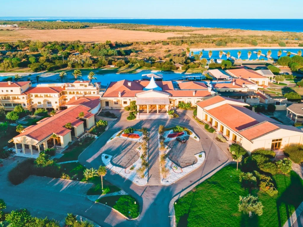 Veduta aerea dell'ingresso del resort con edifici color crema, piazzale e giardini