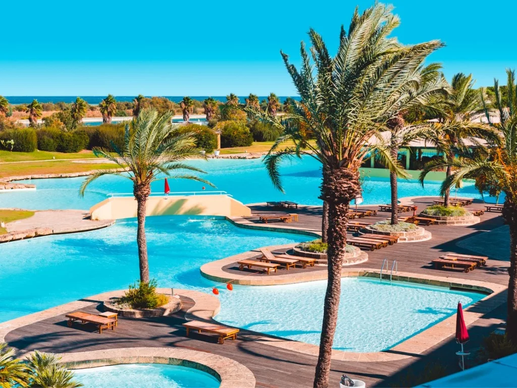 Piscina a laguna con palme e lettini in legno, vista sul mare sullo sfondo