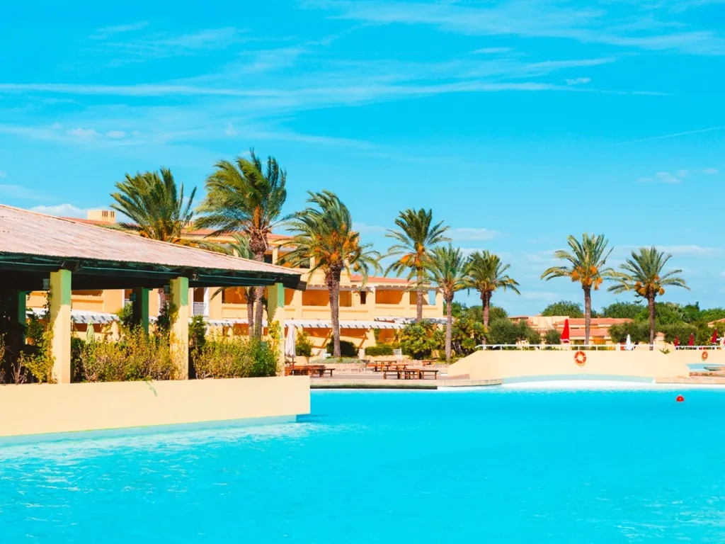 Piscina azzurra con bar coperto, palme e edificio del resort in una giornata soleggiata