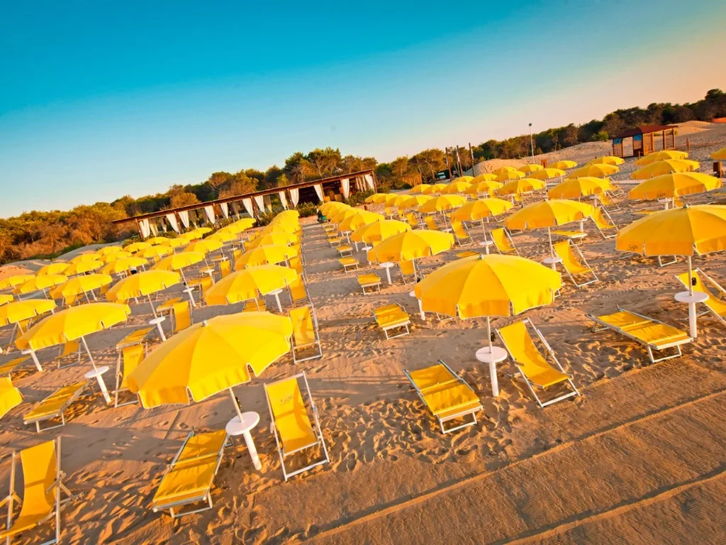 Ombrelloni e lettini gialli sulla spiaggia al tramonto con vegetazione sullo sfondo