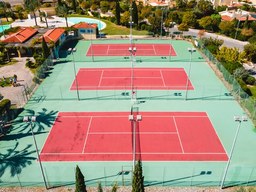 Veduta aerea di tre campi da tennis con edifici e piscina del resort sullo sfondo