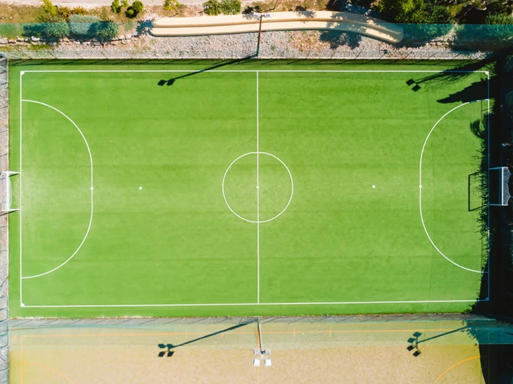 Vista dall'alto di un campo da calcio in erba sintetica verde con segnaletica bianca