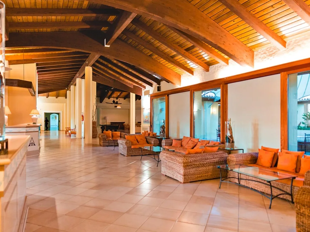 Ampia hall interna con soffitto in legno a travi, divani in vimini e cuscini arancioni