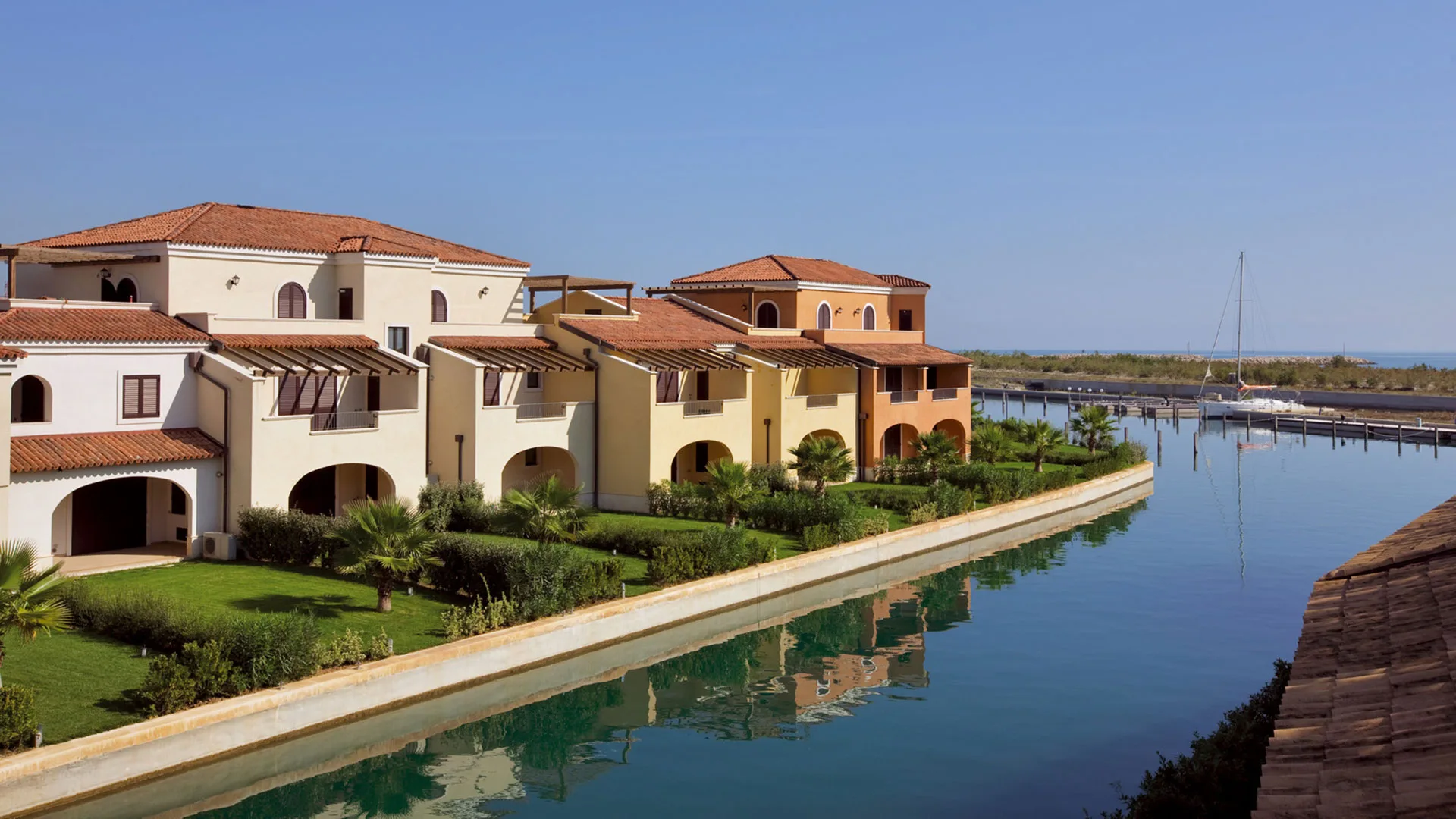 Ville del resort affacciate sul canale con giardini curati, palme e barca a vela ormeggiata