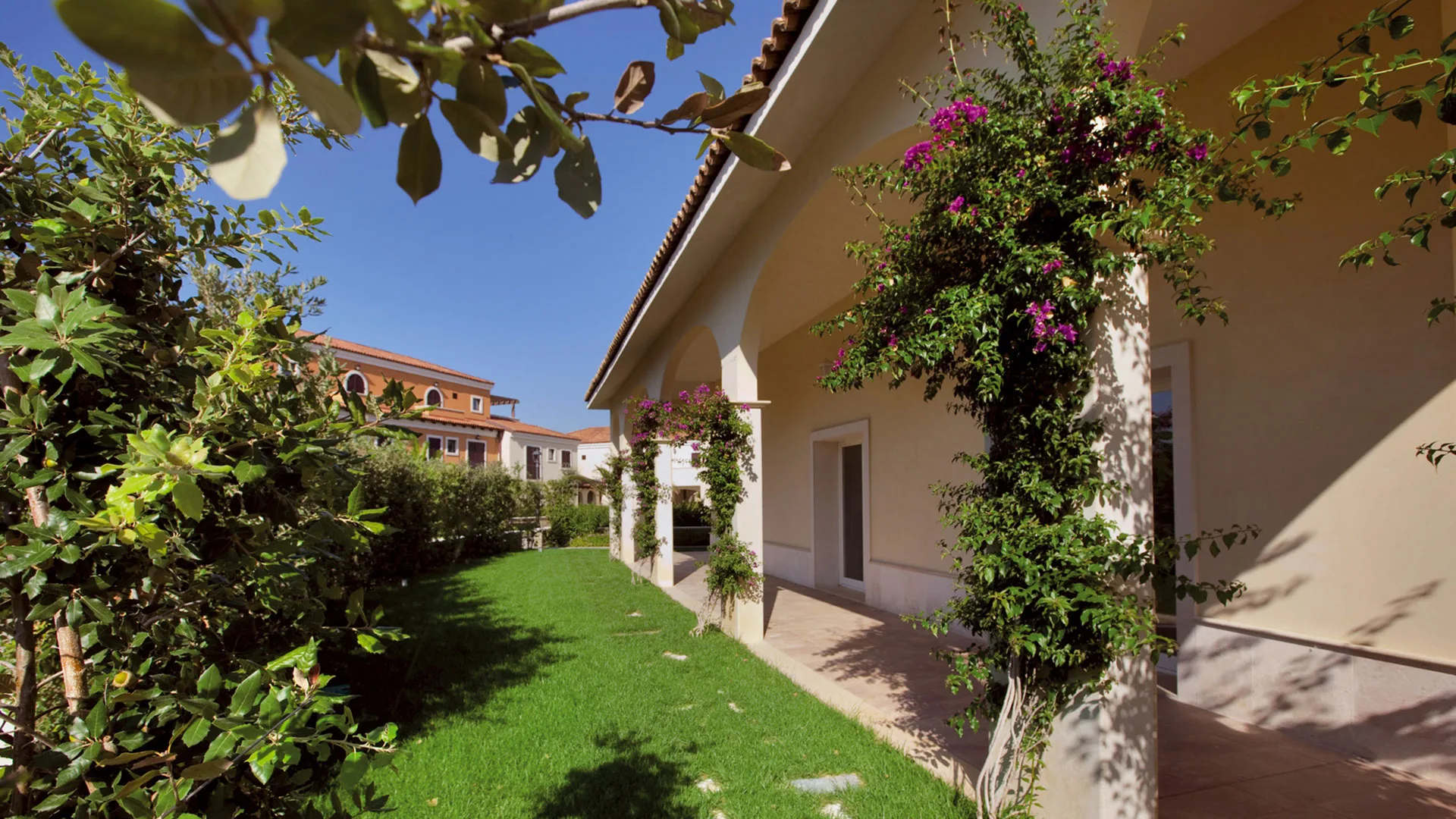 Giardino con prato verde, portici fioriti di bougainvillea e edifici in stile mediterraneo