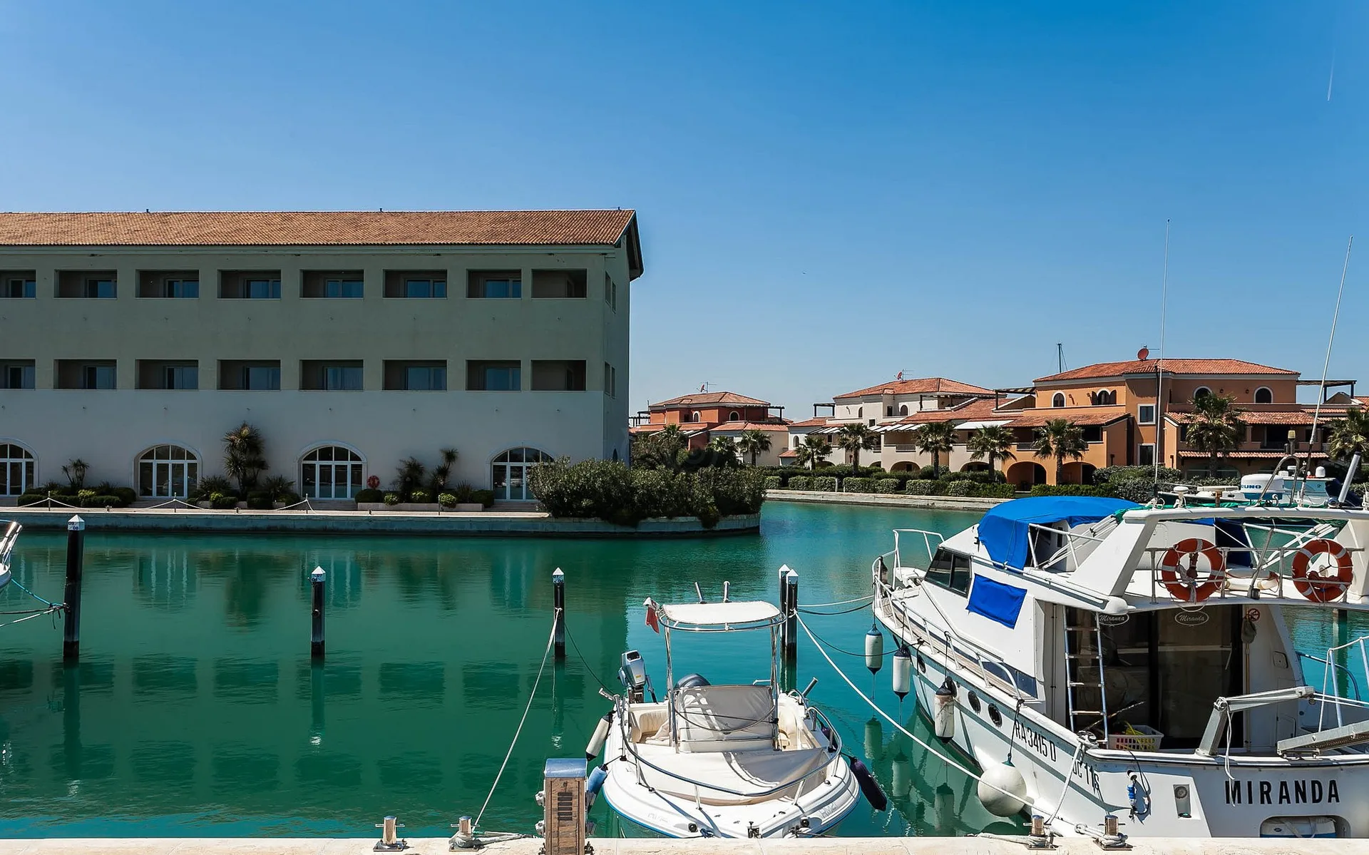 Edificio del resort sul canale con barche ormeggiate al porto turistico sotto cielo azzurro