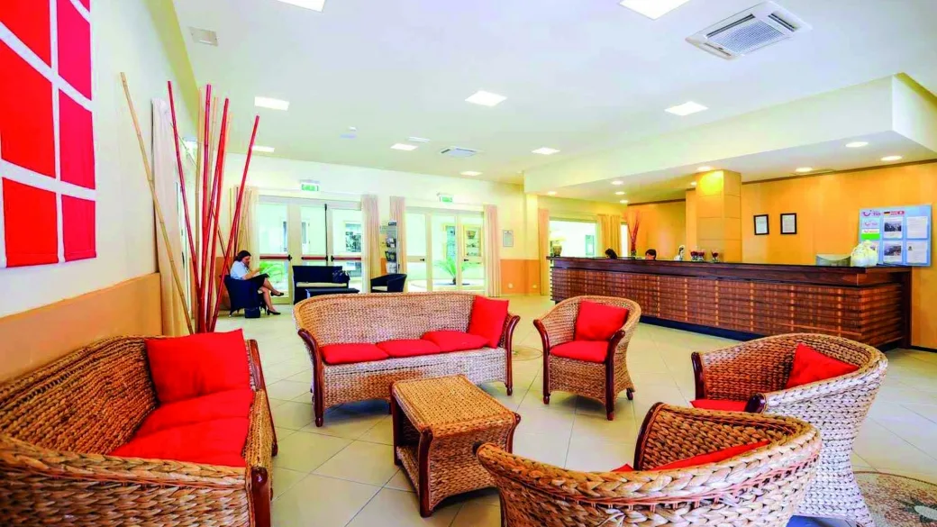 Hall dell'hotel con poltrone in vimini, cuscini rossi e reception