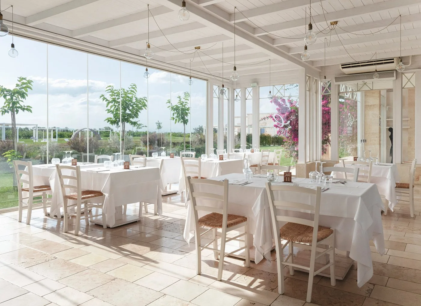 Sala ristorante luminosa con vetrate panoramiche, tavoli bianchi e vista sul giardino