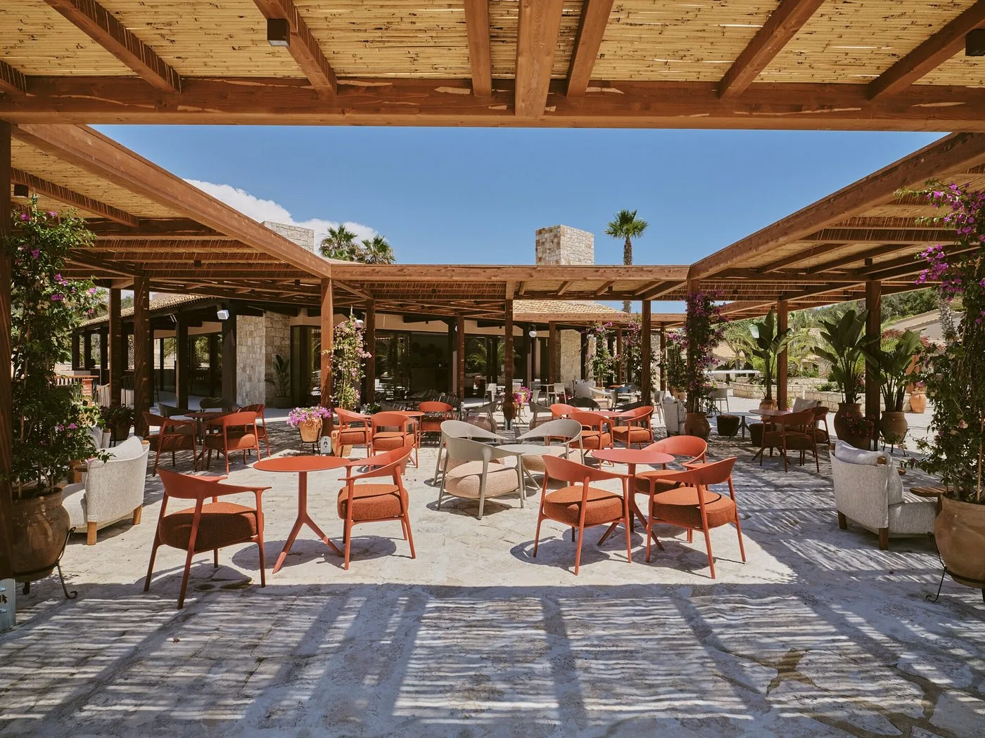 Area ristorante all'aperto con pergolato in legno, tavoli e sedie arancioni