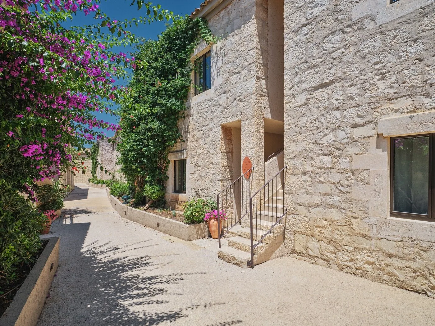 Vicolo in pietra con scalinata, fiori e bougainvillea lungo gli edifici del resort