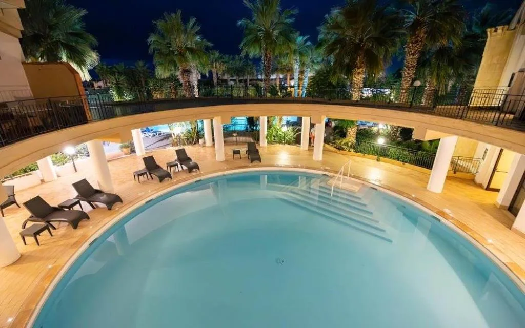 Piscina illuminata di sera con lettini e palme in notturna