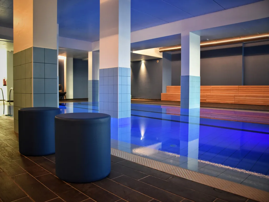 Piscina interna con illuminazione blu, colonne e pouf di seduta