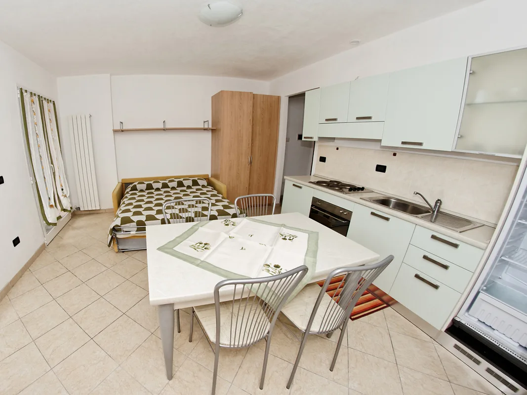 Monolocale luminoso con divano letto, cucina chiara e tavolo da pranzo apparecchiato