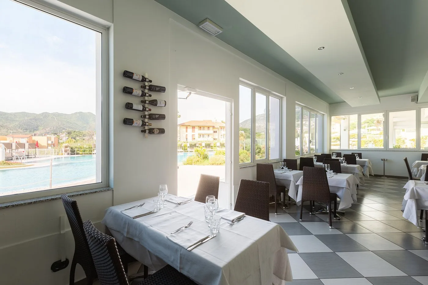 Ristorante interno con ampie vetrate, tavoli bianchi e vista sulla piscina e le montagne